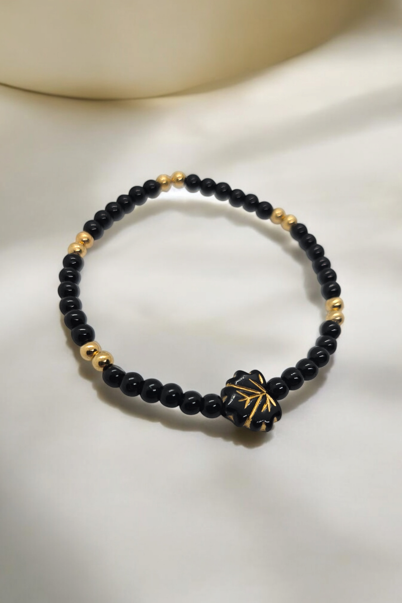 Elastieken armband met zwarte en gouden kralen en een zwart blad