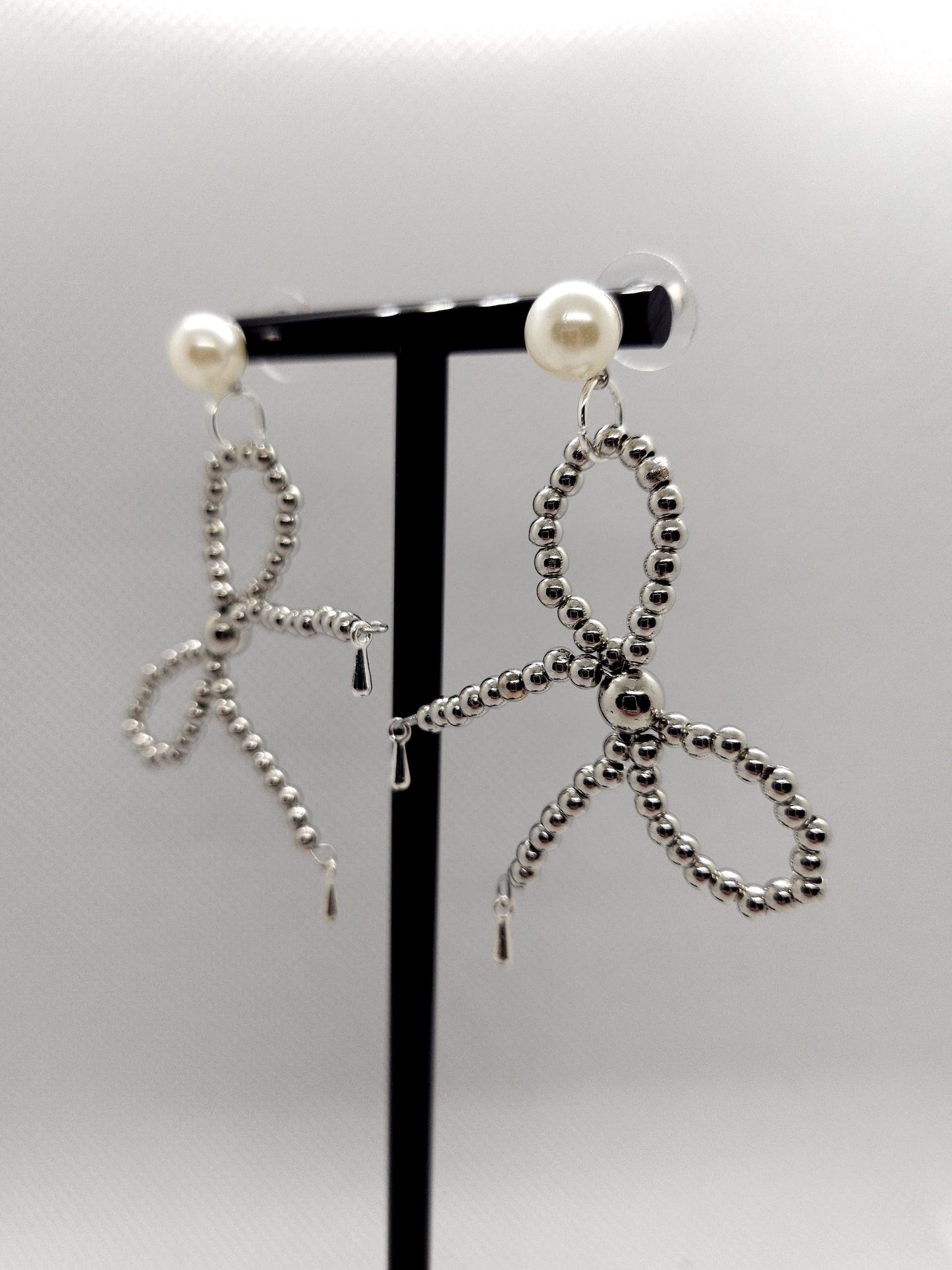 Zilverkleurige oorbellen met zilveren kralen in een strikvorm met parels oorknoppen