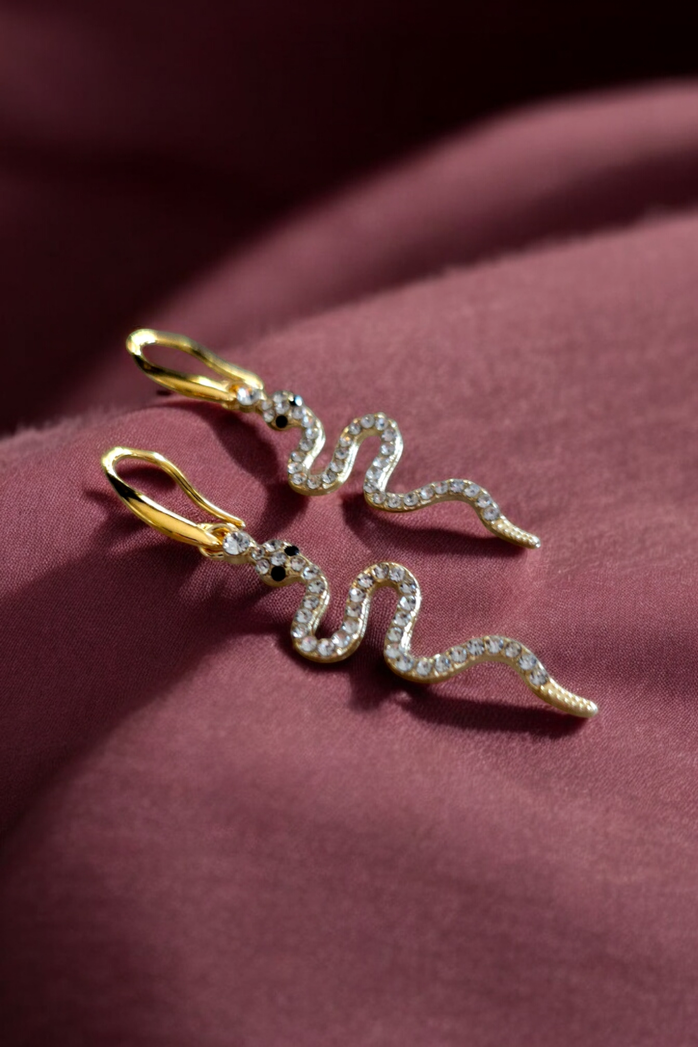 Gouden opvallende oorbellen met een glinsterende hanger in de vorm van een slang