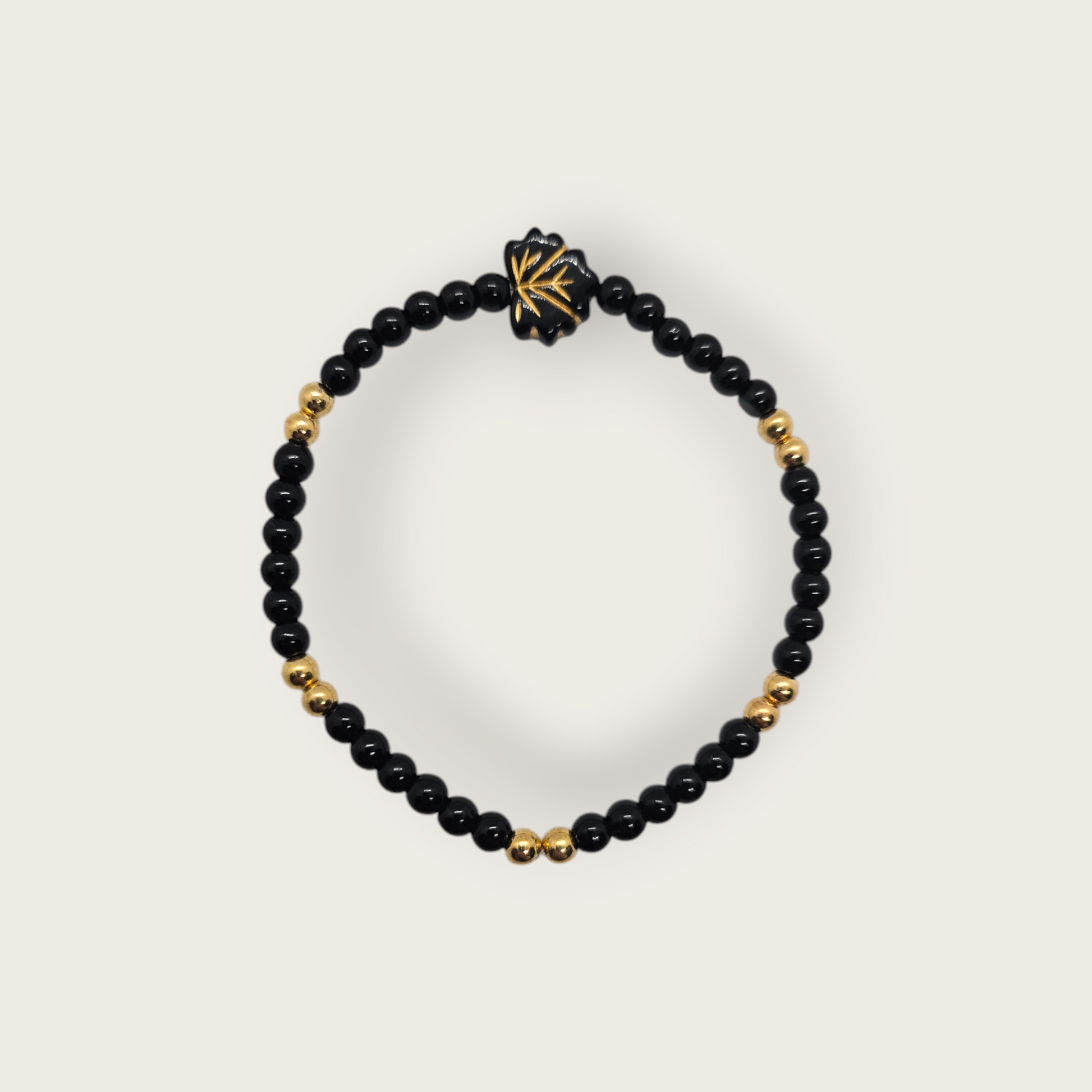 Elastieken armband met zwarte en gouden kralen en een zwarte bladvorminge bedel