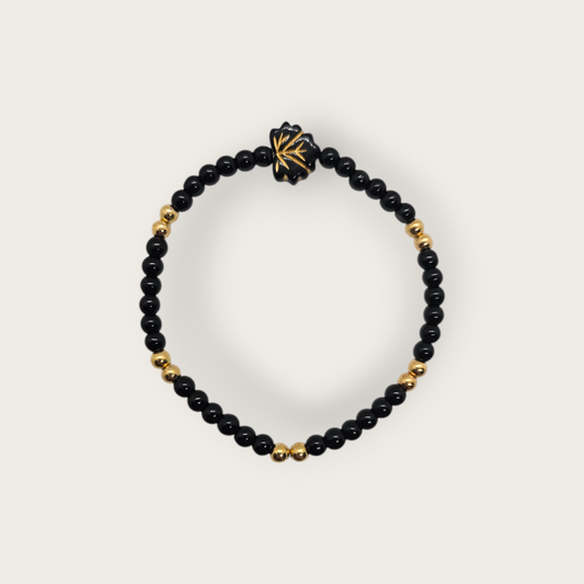 Elastieken armband met zwarte en gouden kralen en een zwarte bladvorminge bedel